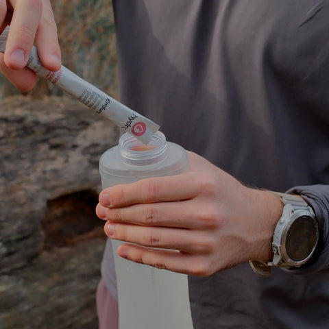 Person pouring in Hydra endura, an electrolyte hydration mix into a soft water bottle outdoors