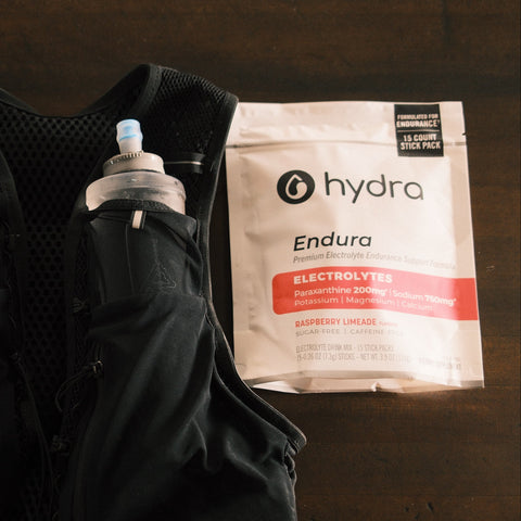 Black hydration vest with two water bottles and a Hydra Endura electrolyte package on a dark surface